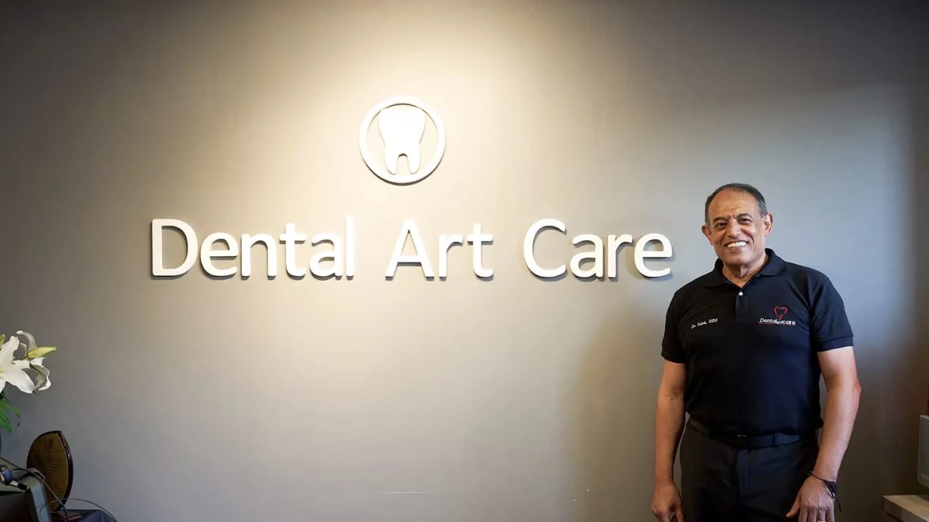Dr. Saleh Elahwal smiling beside the Dental Art Care sign in our Brooklyn office